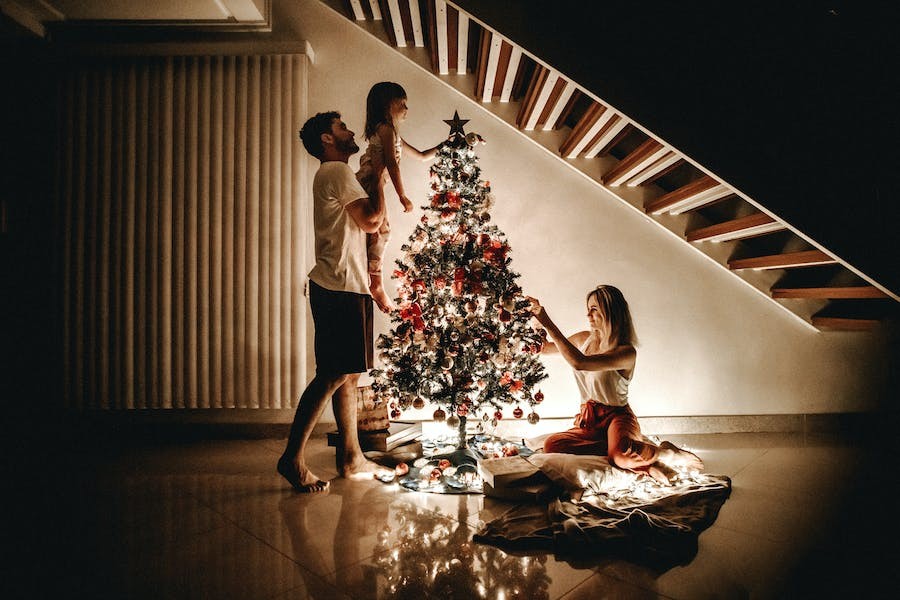 A family decorating a Christmas tree full of lights.