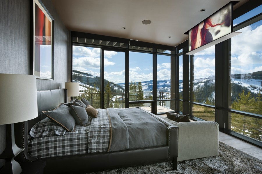 A bedroom with picture windows overlooking the mountains, an in-ceiling speaker, and a TV emerging from the ceiling.