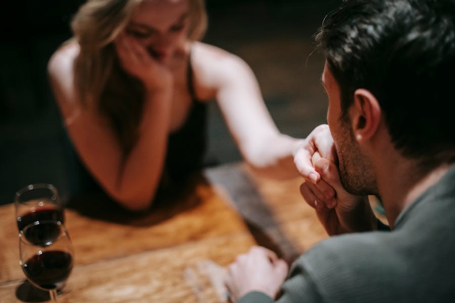 Couple sitting at a wooden table, sharing an intimate moment with two glasses of red wine in the foreground.