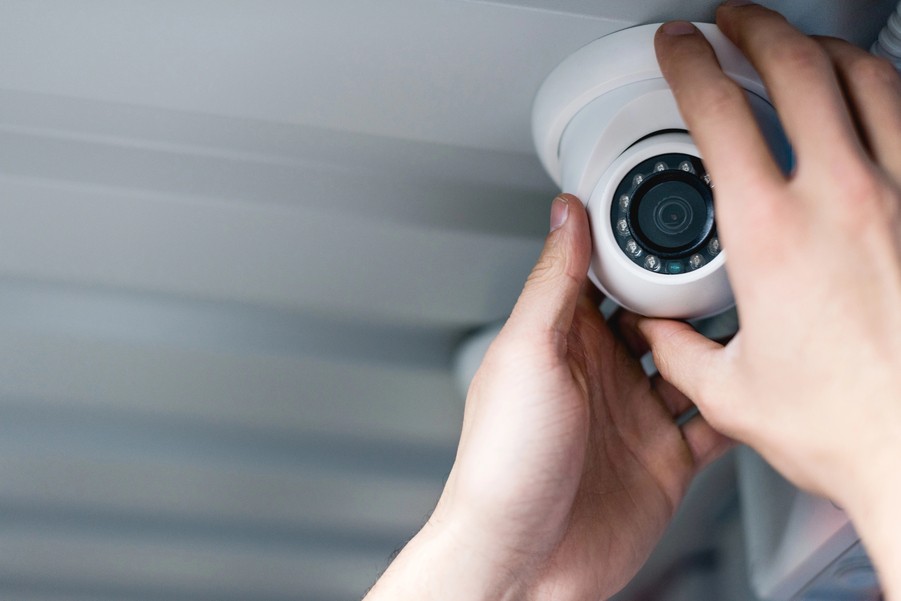 Close-up of hands adjusting a white dome security camera mounted on a ceiling.