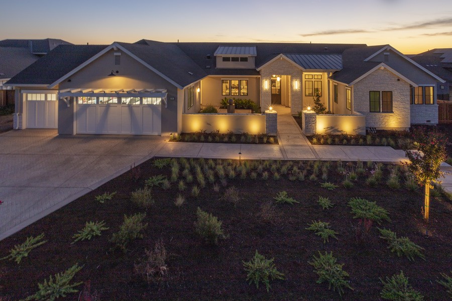 A modern single-story home is illuminated with warm exterior lighting at dusk, highlighting the walkway, garage, and entryway.