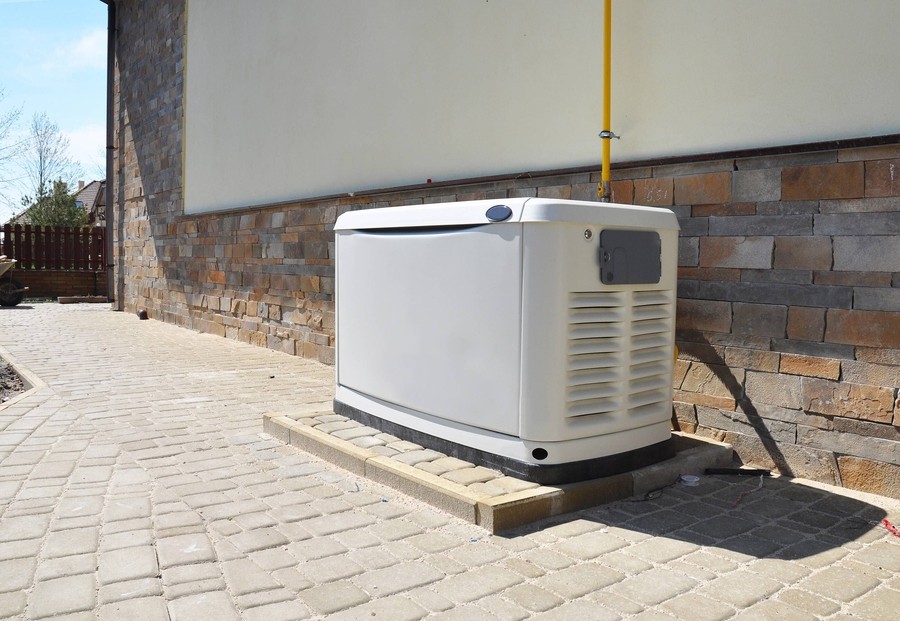 Standby generator installed on a paved area next to a residential building with stone siding.