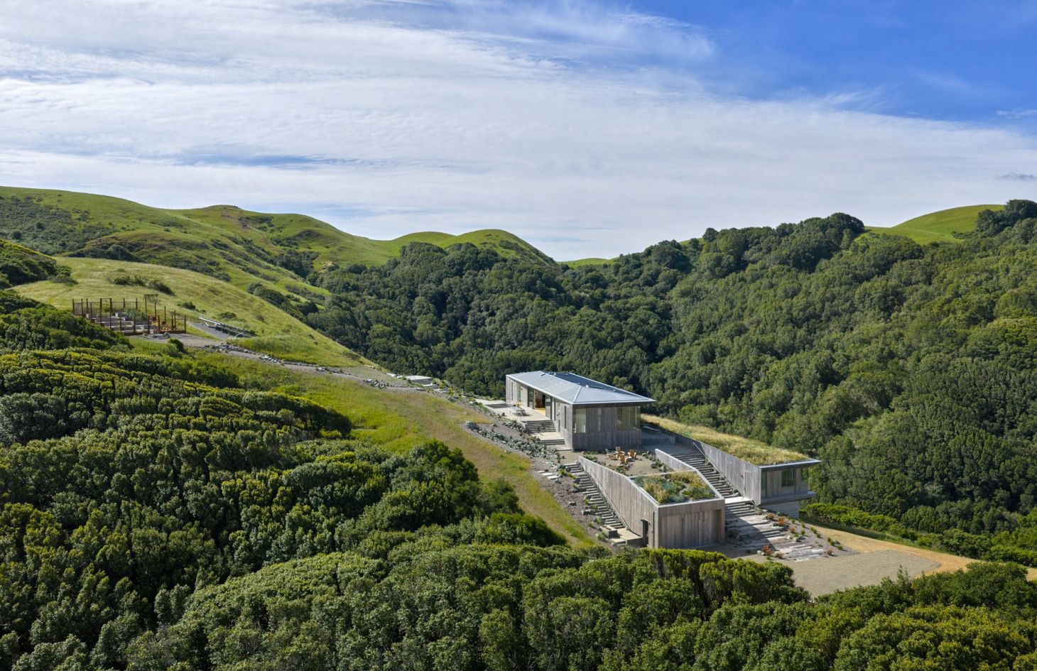 The off-grid estate seen from across the valley among oak-covered hills, with no utility lines running to the property.