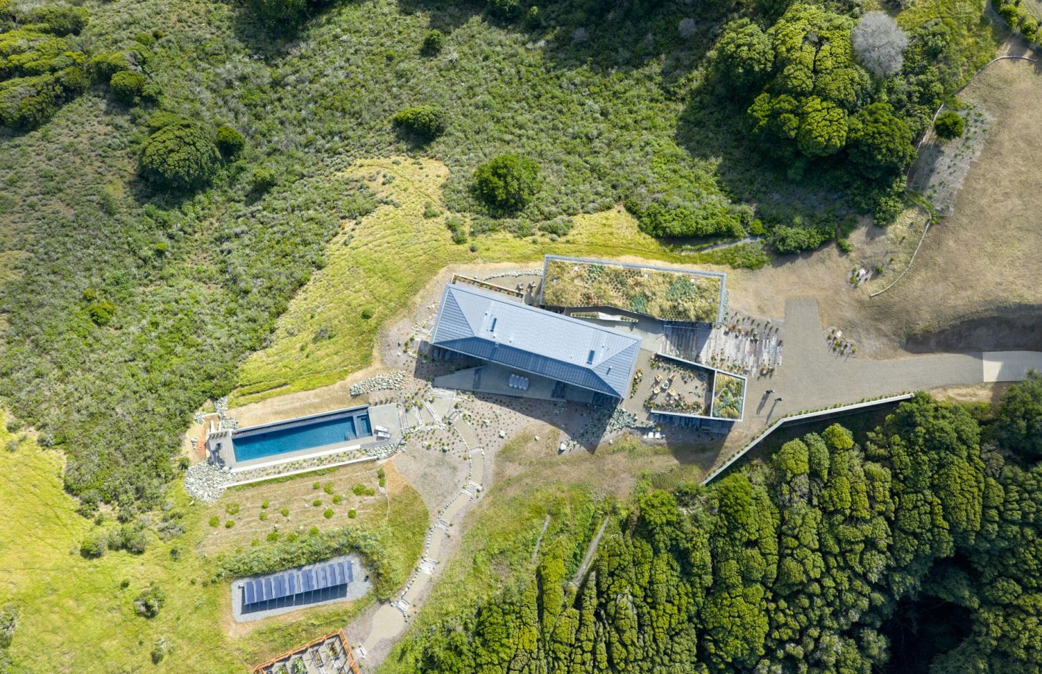 Aerial view of the off-grid Marin County estate on its hillside site, showing the pool and the ground-mounted solar array that powers the home.