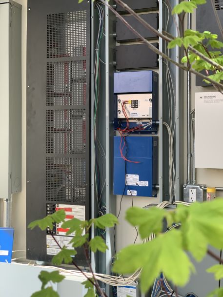 An outdoor utility cabinet containing electrical and low-voltage wiring, control panels, and networking equipment installed on the side of a home.