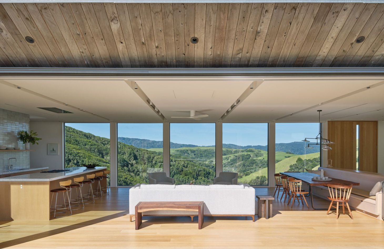 Great room with a wood ceiling and full-height glass framing the hills, with lighting, shades and climate managed by the home control system.