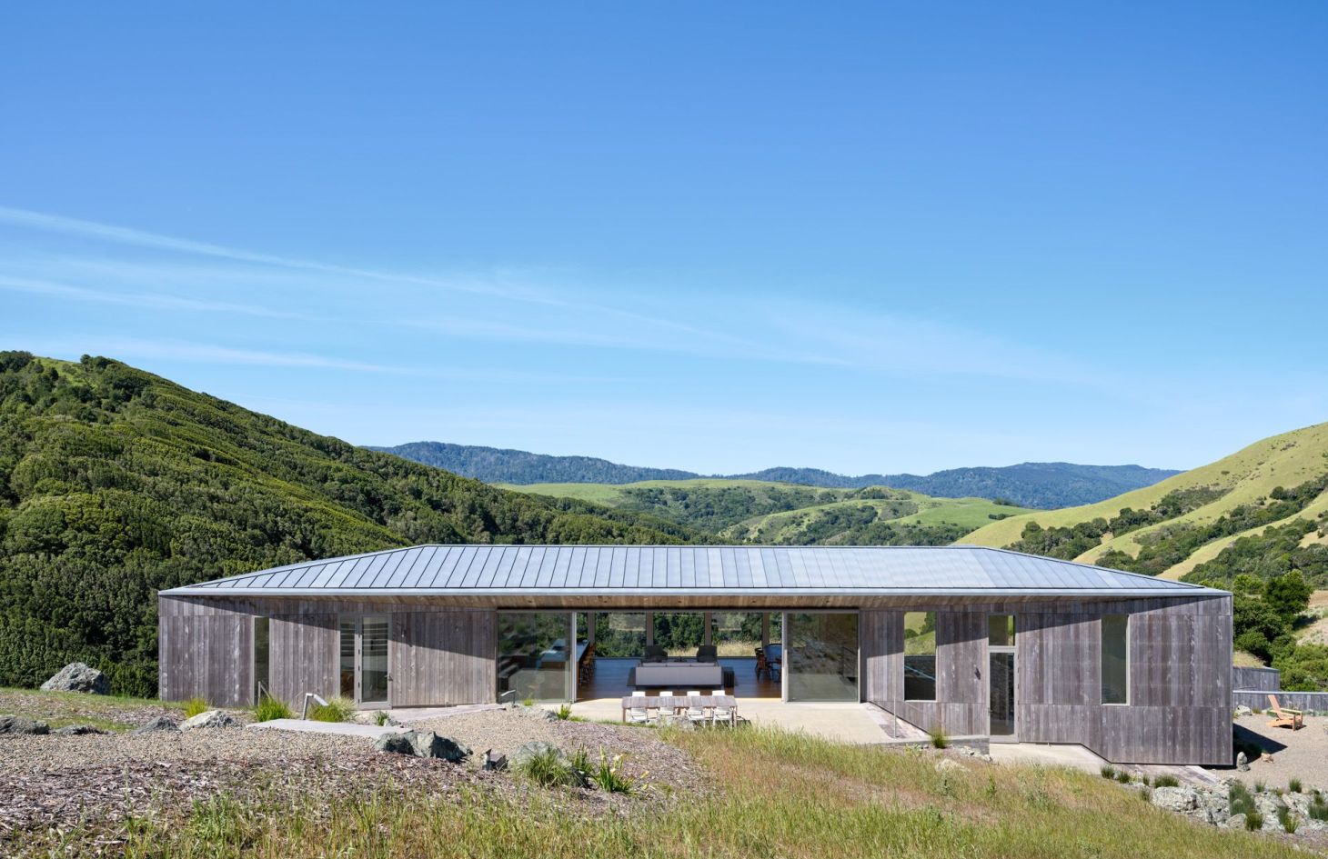 Low-profile wood-clad wing of the off-grid estate rising from a native-grass meadow.