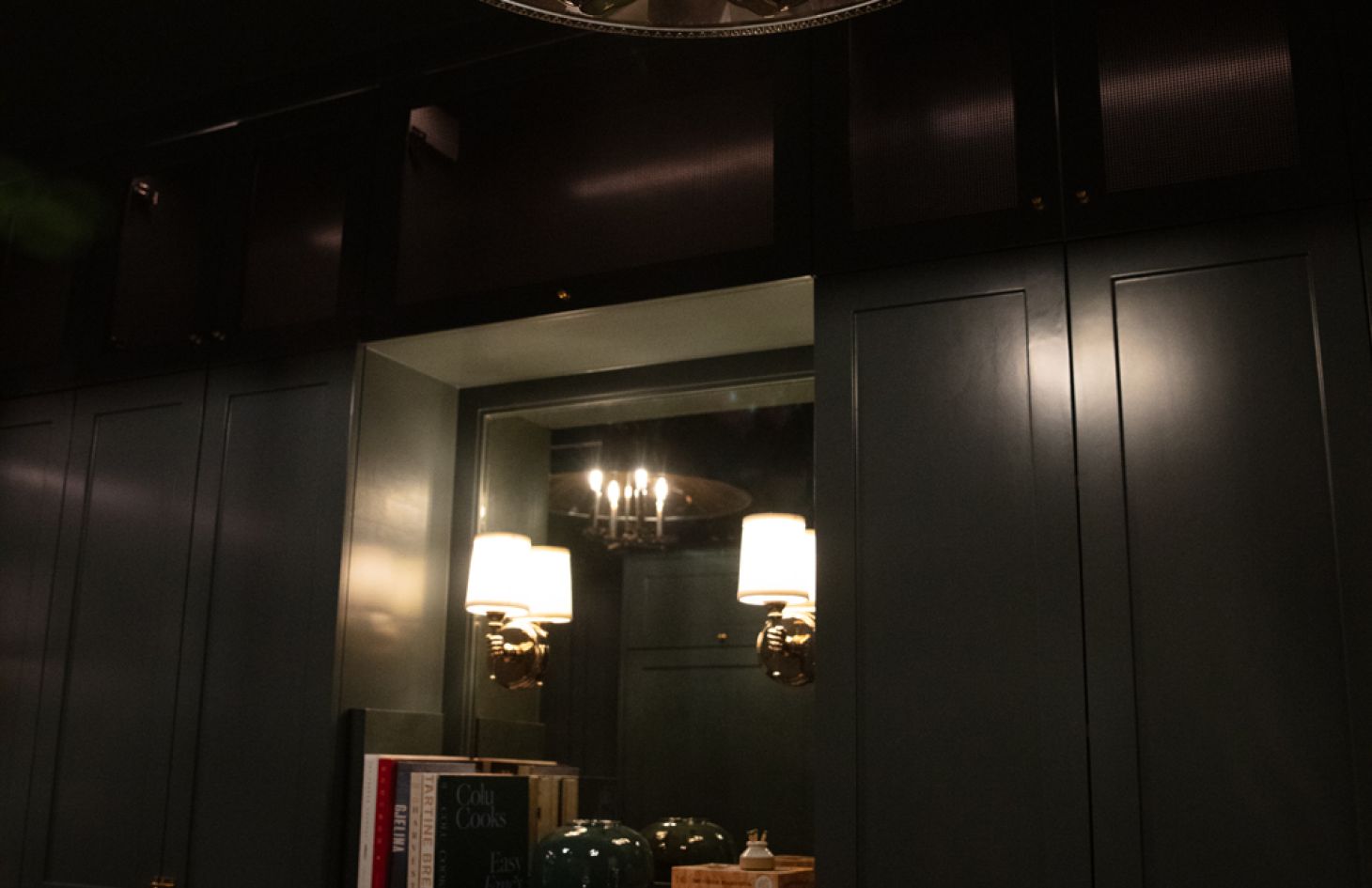 Up-angle of the same green cabinetry showing the reflected chandelier and glowing wall sconces that accent the dark, jewel-toned millwork.