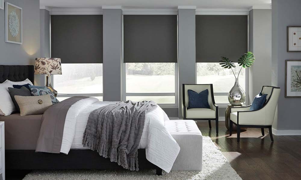 Elegant bedroom with Lutron blackout shades, a cozy bed, and a seating area with armchairs and a decorative vase.